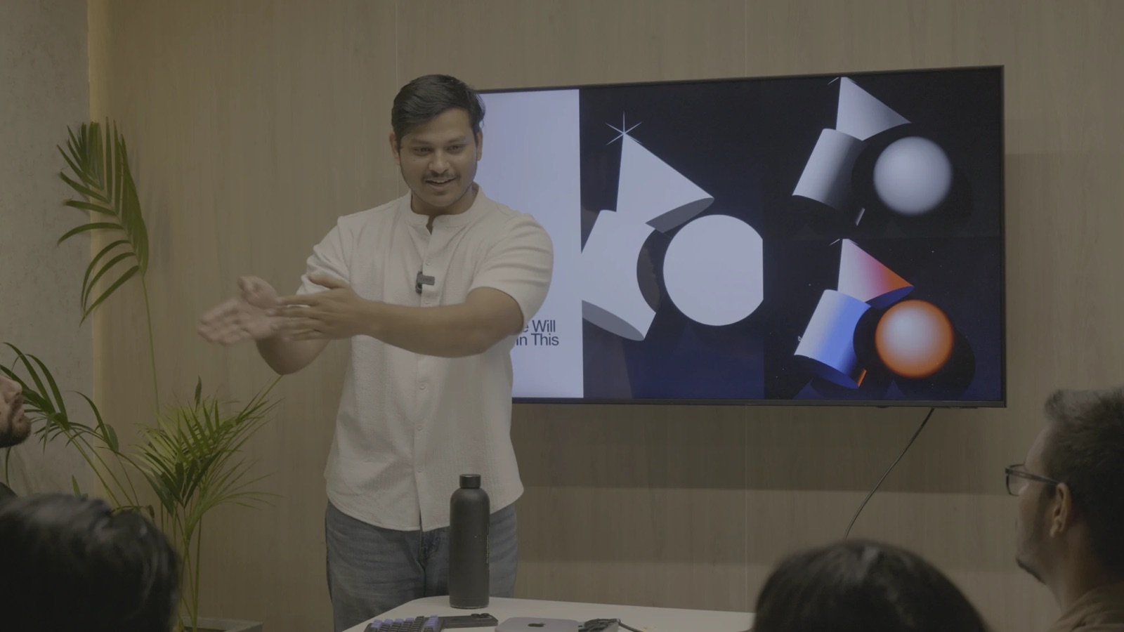 Vivek mid-explanation in front of a screen of 3D shapes, talking to a small group